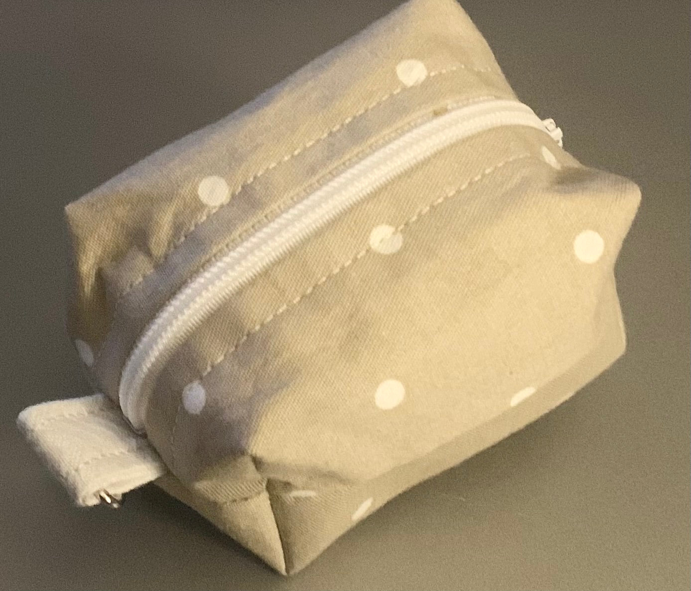 LW Designs poop bag holder in neutral fabric with clip attachment, designed for carrying pet waste bags conveniently.
