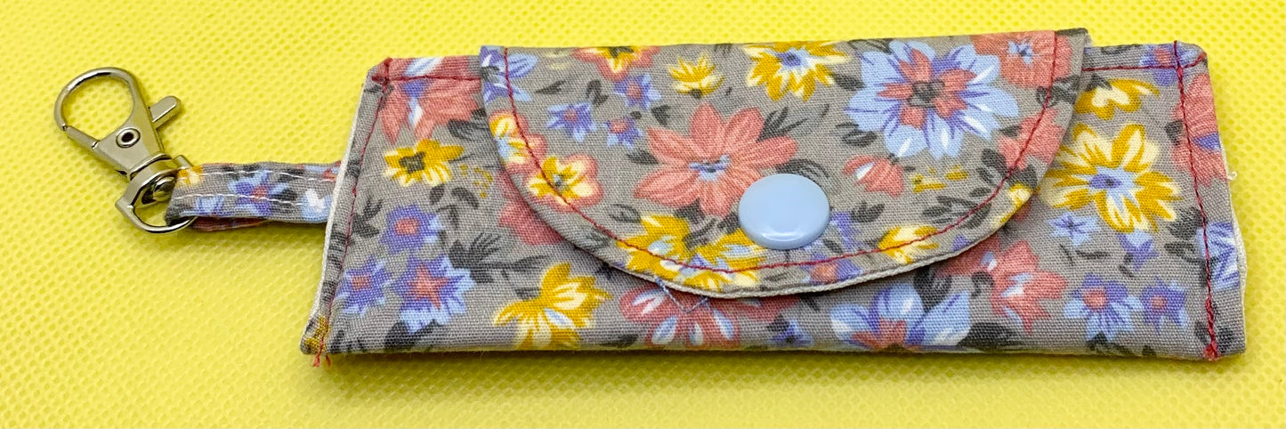 LW Designs lip balm holder in black with a clip, designed to attach to bags or keys for easy access.